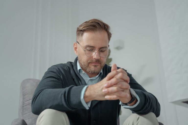 Thuis met een burn-out: man in een grijze trui zit nadenkend thuis in een stoel